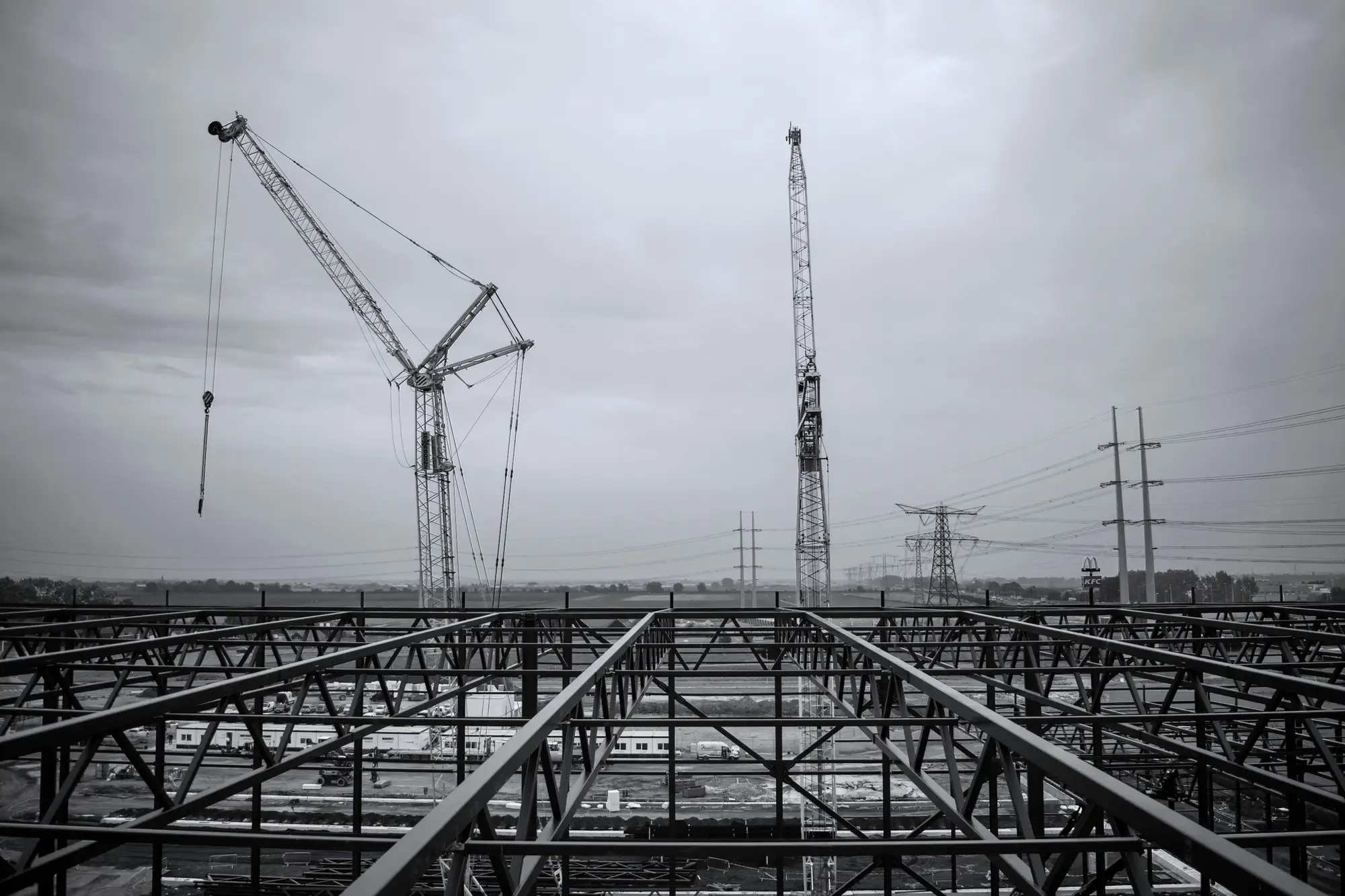 Open steel framing with two cranes behind it on an overcast day